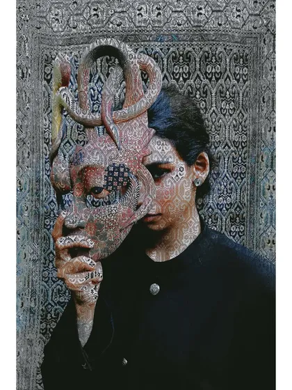 An artistic, digitally manipulated image from 'Roots'. The pattern of the background tapestry is overlaid on the model and the mask, visually merging person, culture, and art.