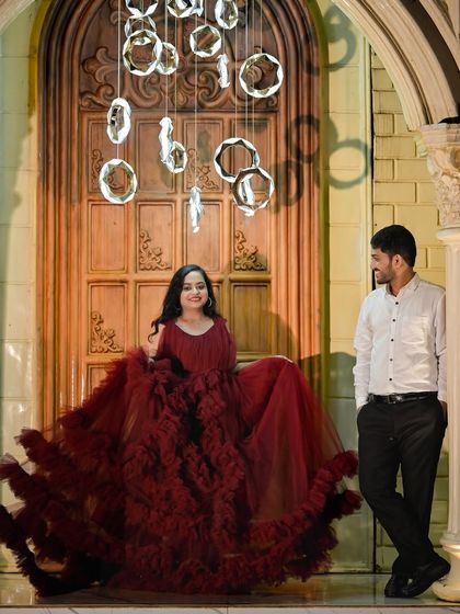A stylish couple poses in front of a grand door, with hanging ring lights creating a modern and sophisticated atmosphere.