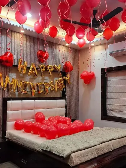 A full-on romantic anniversary surprise with a room filled with red balloons. The setup includes 'Happy Anniversary' foil letters above the bed and helium balloons floating to the ceiling, creating an immersive and celebratory feel.