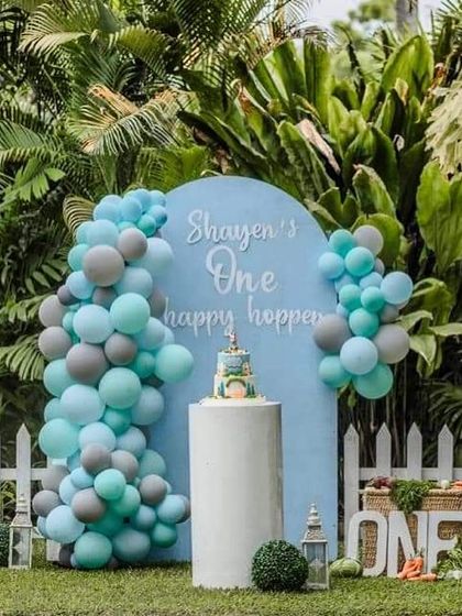 A lovely Peter Rabbit theme for a "happy hopper" first birthday. This outdoor setup features a gentle blue and grey color scheme, a custom backdrop, and a white picket fence.