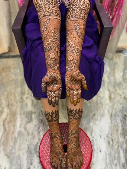 A full view of a bridal mehendi session, showing the intricate work on both the hands and feet. The leg design features a simple forest-like border which is very unique.