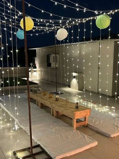 A beautiful night shot of the fairy light canopy and low seating arrangement, perfect for a relaxed and magical birthday dinner.