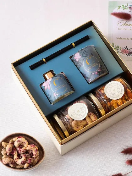 Light up your celebrations with this special hamper. It features a fragrant candle, a luxurious room fragrance, and two of our gourmet nut varieties: crunchy Rose Cashews and flavorful Thai Curry Nuts.