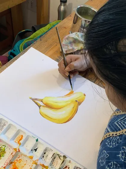 A student paints a bunch of bananas in watercolor. Mastering the natural colors and textures of fruits and vegetables is a beautiful challenge that our students embrace.