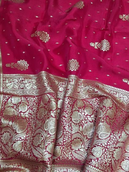 The rich texture and vibrant color of a Banarasi saree. This close-up shows the detailed floral and leaf patterns woven with golden thread on a bright pink base, a testament to the weaver's skill.