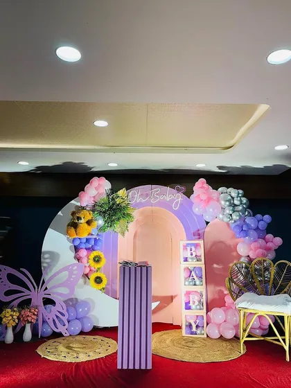A butterfly-themed baby shower setup featuring a large lavender butterfly cutout and a wicker peacock chair. The round backdrop includes a photo frame section to display sonogram pictures or maternity photos.