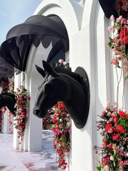 A wall of black horse-head sculptures emerging from white arches, adorned with beautiful pink and red flowers. This dramatic installation served as a stunning photo backdrop.
