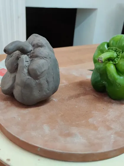 An un-fired capsicum sculpture sits next to its inspiration. The student did a wonderful job capturing the organic lumps and bumps of the real vegetable.