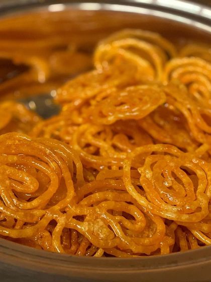 A close-up of our perfectly golden jalebis, soaked in sweet syrup. This classic Indian dessert is a must-have for celebrations, and we make sure each one is crispy and delicious.