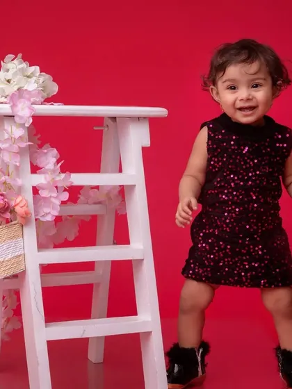 The same portrait in vibrant color, with the toddler's sparkly dress standing out against the bold red background. Her joyful expression is the highlight of the shot.
