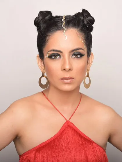 An artistic look with gold detailing on the forehead and a bold red outfit. The space buns add a modern, edgy feel.