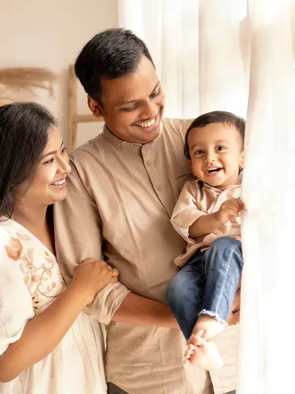 A happy family of three, their faces lit up by the natural light from the window.