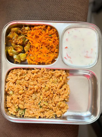 A colorful meal of tomato rice, ivy gourd palya, carrot salad, and raita. The variety of vegetables provides a wide range of vitamins and antioxidants.