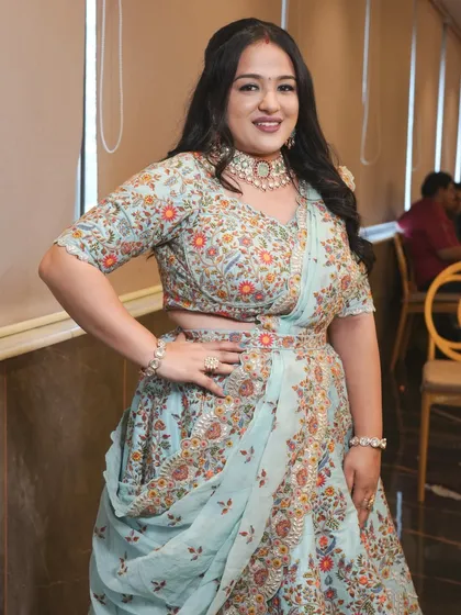 A full-length shot of a happy client at a wedding celebration. Her pastel blue floral lehenga is perfectly paired with a kundan choker, creating a fresh and elegant festive look.