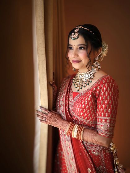 A thoughtful portrait of a bride by the window in her red lehenga. The natural light highlights the beautiful craftsmanship of the rental outfit.