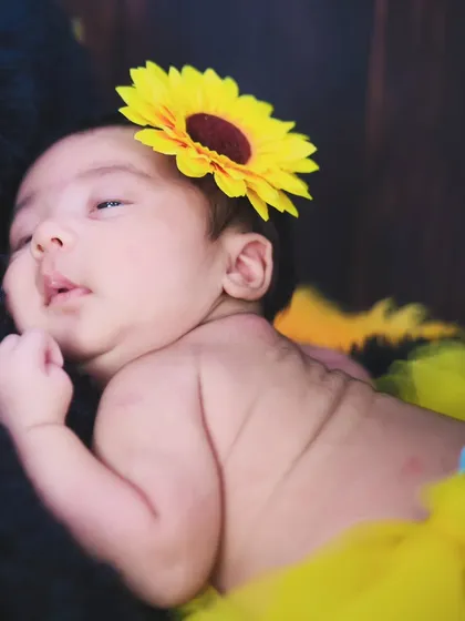 A newborn rests peacefully, adorned with a sunflower headband. We use simple floral props to add a bright and cheerful touch to our sessions.