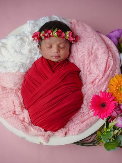 A rainbow of flowers. This baby, swaddled in red, is surrounded by a beautiful array of colorful flowers, creating a vibrant and joyful portrait.