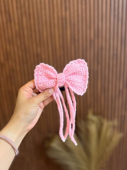 This adorable pink crochet bow comes with long tassels for a playful touch. It's attached to a hair tie for easy styling.