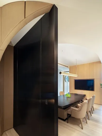 The curved, dark metal door of the conference room provides a strong contrast to the light wood paneling, creating a dramatic entryway into the meeting space.