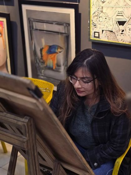 A student takes a moment to study her reference before continuing with her detailed ballpoint pen drawing.