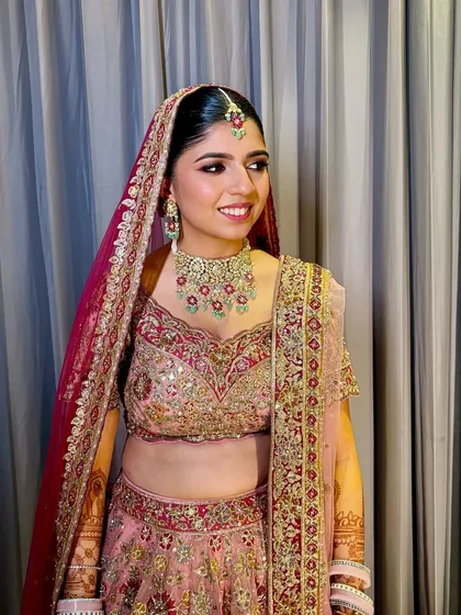 A touch of makeup, a touch of magic. This gorgeous bride on her wedding day, radiant in a pink and gold lehenga with a classic red rose bun.