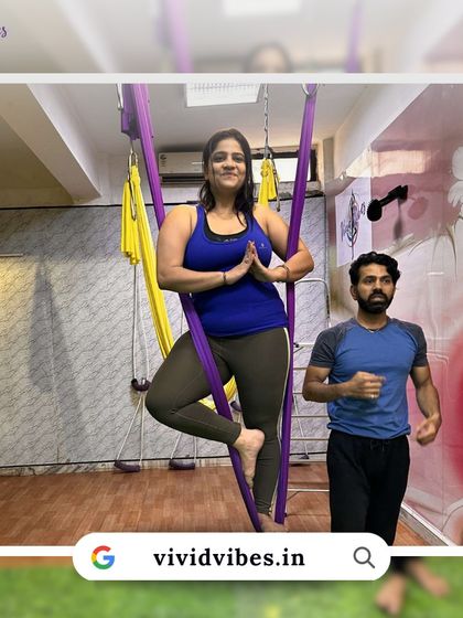 Taking your practice to new heights, one step at a time. This student is learning the tree pose in the hammock with an instructor nearby for support.