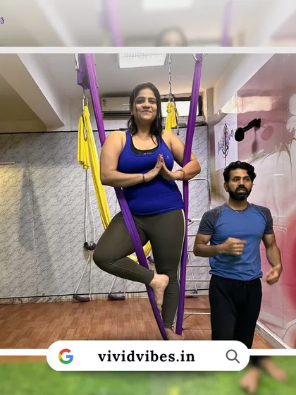 Taking your practice to new heights, one step at a time. This student is learning the tree pose in the hammock with an instructor nearby for support.