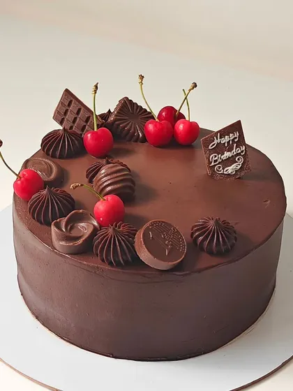 A classic and decadent chocolate truffle cake, topped with fresh cherries and a variety of chocolate garnishes. A timeless choice for any celebration.