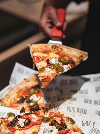 A perfect slice, lifted and ready to be devoured. This pizza is topped with jalapeños, sundried tomatoes, and feta, offering a mix of spicy, tangy, and salty flavors.
