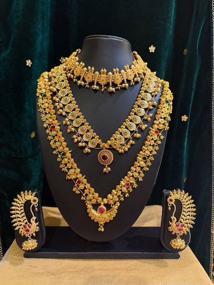 A traditional set with intricate peacock motifs and red stones, including a choker, a layered necklace, and jhumkas.