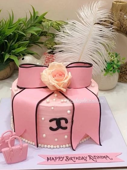 A chic Chanel-themed cake for a fashion lover's birthday. This pink ganache cake is decorated with a fondant bow, the Chanel logo, and mini handbags.
