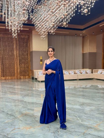 A solo shot in a beautiful blue saree at a grand event venue. Ready to mingle and host.