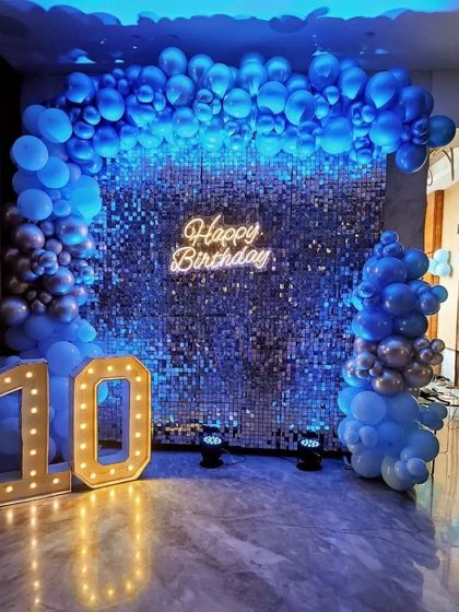 A striking 10th birthday party with a blue shimmer wall. The wall is framed by a blue and silver balloon arch and accented with large marquee numbers.