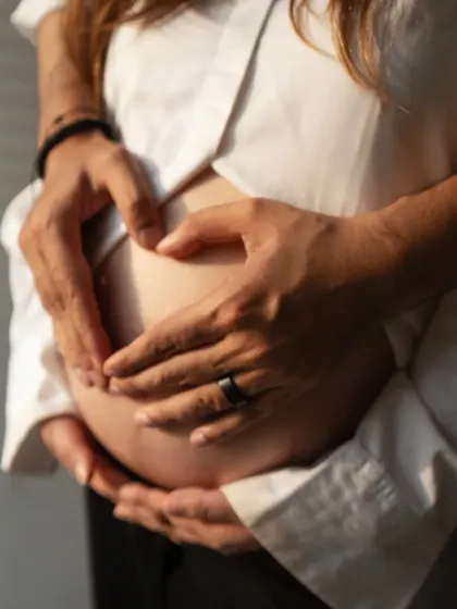 A symbol of love. The couple's hands form a heart shape on the baby bump, a simple yet profound gesture captured in a beautifully lit, close-up photograph.
