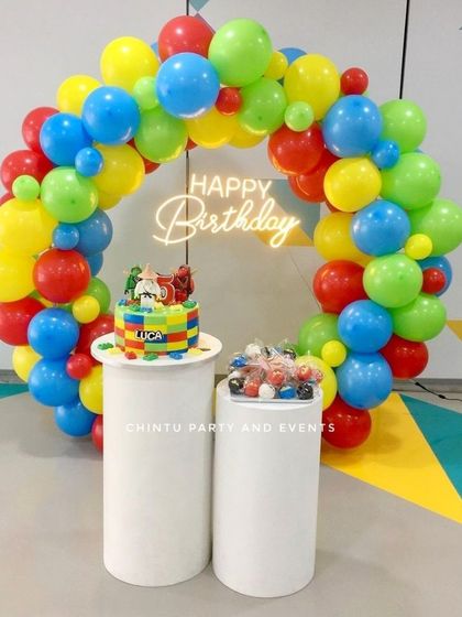 A simple and colorful balloon arch in primary colors of red, yellow, blue, and green. This versatile setup includes pedestals for a cake and treats and works for any cheerful birthday celebration.