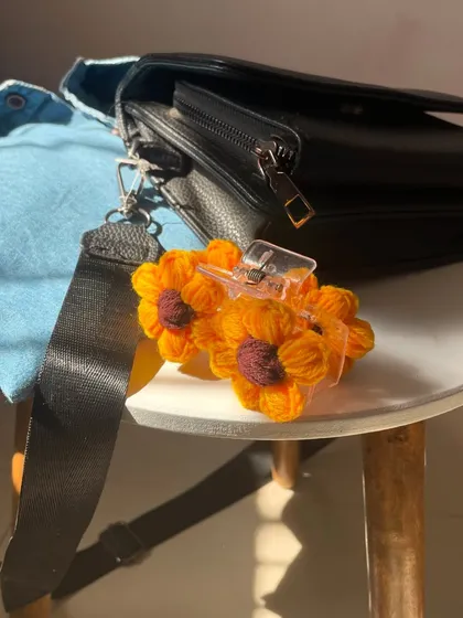 A crochet sunflower claw clip, casually attached to a handbag. It's a versatile accessory that can add a pop of color and fun to more than just your hair.
