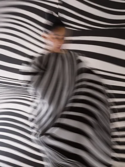 Using a slow shutter speed to capture the movement of the pleated dress against the static background. This technique turns the graphic campaign into a dynamic, abstract image.