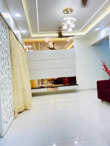 A wide view of a living room showing the TV unit with a reflective bronze panel and a decorative jaali partition. The false ceiling design with cove lighting adds depth and a sense of luxury to the space.