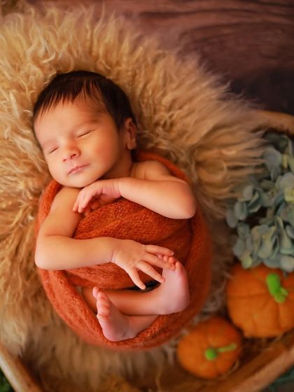A close-up of a newborn wrapped in a rustic orange swaddle, perfectly curled up in a prop filled with soft fur. This pose emphasizes the baby's flexibility in the first few weeks.