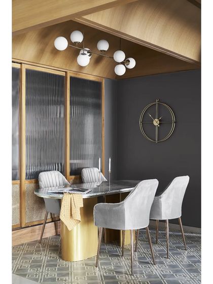 The bespoke dining table features a botanic green marble top and brass-cladded supports, set on geometric cement tiles. This combination of materials adds a layer of luxury and custom detail.