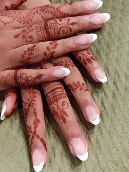 A timeless French manicure on almond-shaped nails, perfectly complementing the beautiful, intricate mehendi design for a bridal look.