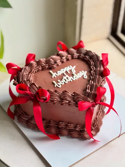 A full view of the rich chocolate heart cake, adorned with intricate piping and vibrant red ribbons for a classic birthday statement.