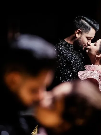 An intimate, stolen kiss amidst the chaos of the party, captured from a distance.