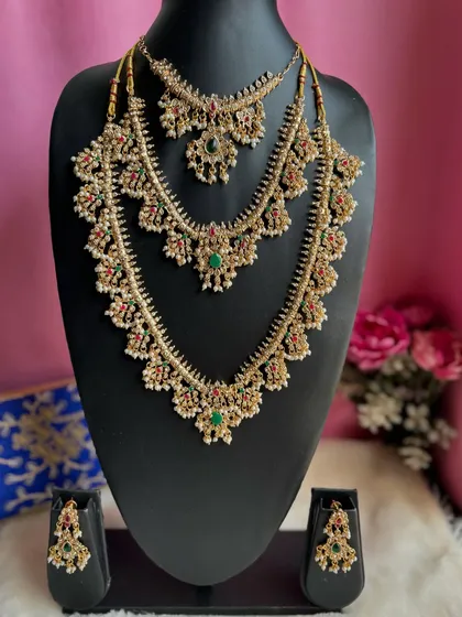 A layered bridal necklace set with red and green stones and pearl details. This three-piece necklace set provides a full, grand look for a bride.