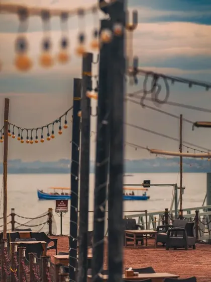 A wide-angle view of a couple on a pier, framed by string lights. This shot captures the beautiful ambiance of a seaside location and the feeling of a private, romantic moment.