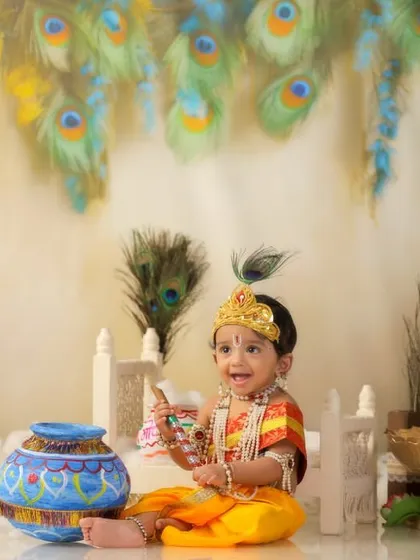 A joyful shot of baby Krishna laughing, holding his flute, with a backdrop of peacock feathers and festive decor.