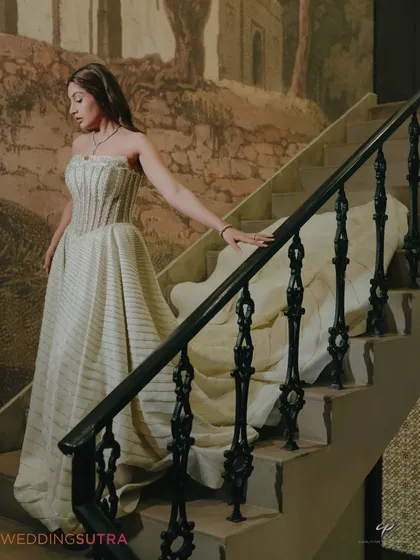 An elegant portrait of the bride descending a staircase, her gown flowing behind her. This image has a timeless, almost painterly quality, perfect for an editorial pre-wedding album.