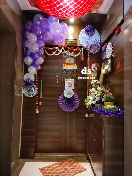 We decorated this home entrance to welcome a new baby. The decor includes a balloon garland, paper fans, a traditional toran, and floral arrangements, creating a warm and festive entryway for guests.