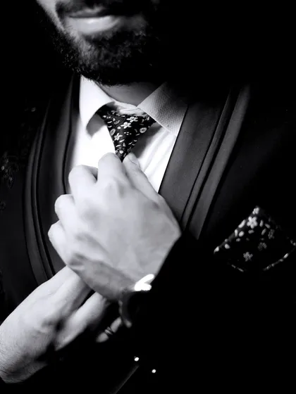A detailed, artistic black and white shot of the groom adjusting his tie. This focuses on the small details that complete the look.