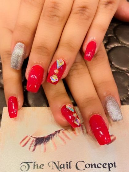 A bright and bold set of red square nails. The look is elevated with silver glitter accent nails and geometric iridescent stones on the middle fingers.